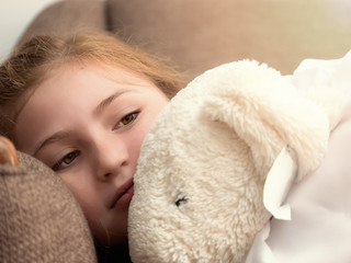 Cute caucasian blonde girl kid laying on sofa with doll feeling happy