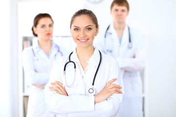 Happy female doctor keeping medical clipboard while medical staff are at the background