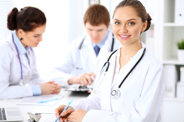 Happy female doctor keeping medical clipboard while medical staff are at the background