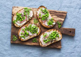 Cream cheese, green peas, radishes and micro greens spring sandwiches on a cutting board. Healthy eating, slimming, diet lifestyle concept. On a blue background, top view