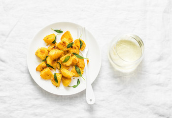 Crispy polenta crust potatoes baked with sage butter and a glass of white wine on a light background, top view
