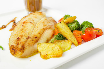 Grilled fish fillets steak served with mix vegetable, potatoes and a glass of black pepper gravy sauce on white background