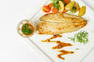 Grilled fish fillets steak served with mix vegetable, potatoes and a glass of black pepper gravy sauce on white background