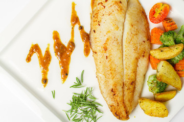 Grilled fish fillets steak served with mix vegetable, potatoes and a glass of black pepper gravy sauce on white background