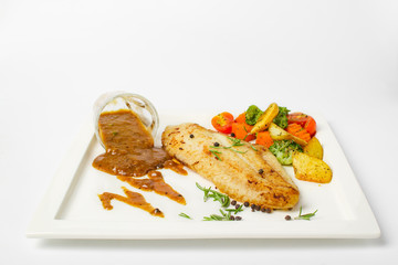 Grilled fish fillets steak served with mix vegetable, potatoes and a glass of black pepper gravy sauce on white background