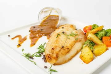 Grilled fish fillets steak served with mix vegetable, potatoes and a glass of black pepper gravy sauce on white background