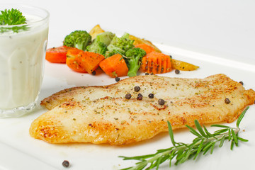 Grilled fish fillets steak served with mix vegetable, potatoes and a glass of white cream sauce on white background