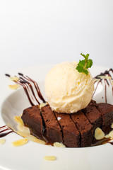 Homade chocolate brownies topped with vanila ice cream in white plate on white background