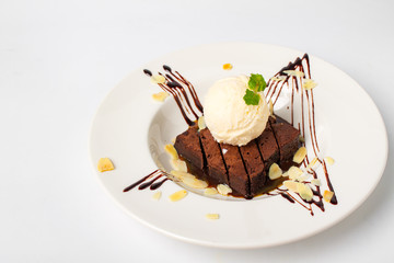 Homade chocolate brownies topped with vanila ice cream in white plate on white background