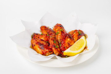 Grilled chicken wings with BBQ sauce. Garnish with lemon and coriander in a paper top view closeup on white background