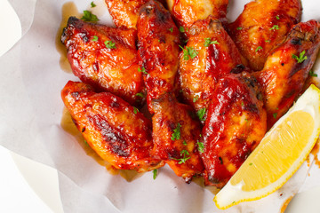 Grilled chicken wings with BBQ sauce. Garnish with lemon and coriander in a paper top view closeup on white background