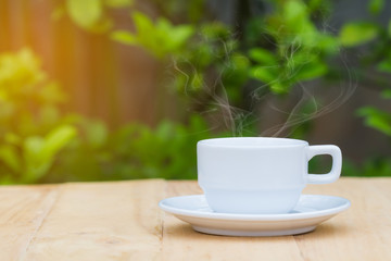 hot coffee on wooden table with blurred green plant background. Copyspace