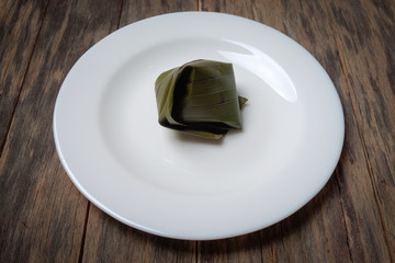 Koci the malay glutinous rice ball served in banana leaf on white plate over wooden table
