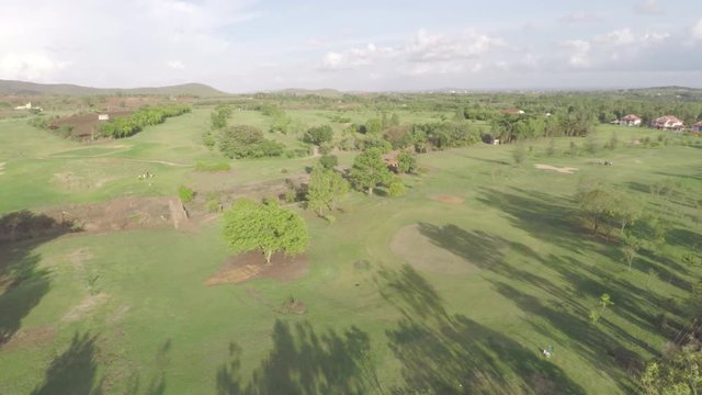 A scenic aerial view of a golf course with shadows of trees near a farm in India.