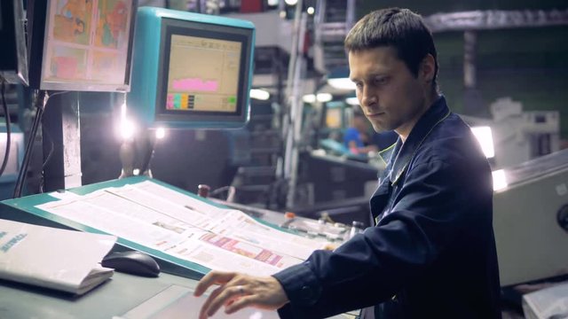 Worker at industrial computerized machine operating with factory line.