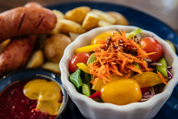 Two grilled bratwurst sausages with potato, vegetable salad and sause