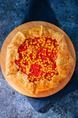 Tomato and sweet corn galette on a wooden board. Top view. Blue stone background.