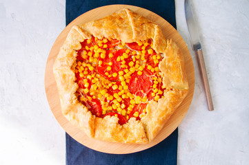 Tomato and sweet corn galette on a wooden board. Top view. White stone background.