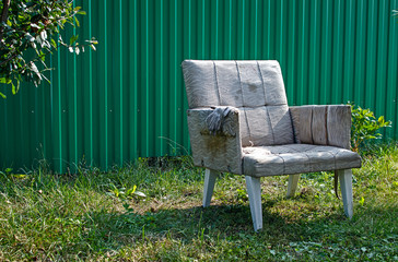 An Old Shabby Armchair Against The Backdrop Of A Green Fence.