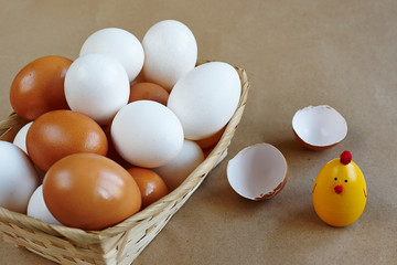 toy chicken, basket in eggs, broken shell on brown background