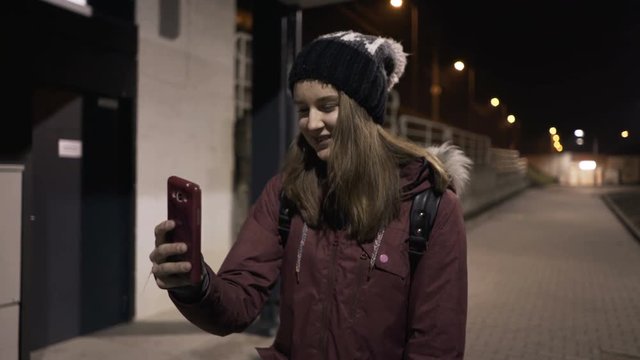 Happy teenage girl chatting on smartphone in city at night

