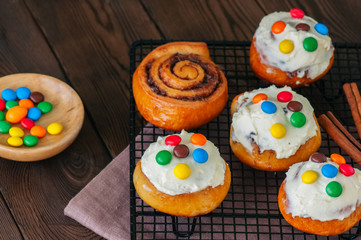 Classic cinnamon rolls - cinnabons with cream cheese frosting with smarties. Wooden background.