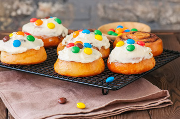 Classic cinnamon rolls - cinnabons with cream cheese frosting with smarties. Wooden background.