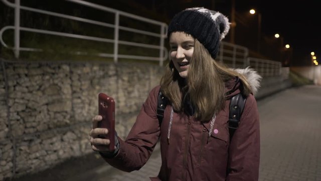 Happy teenage girl chatting on smartphone walking in city at night

