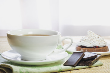 Obraz na płótnie Canvas A cup of tea, pieces of chocolate and a chocolate cake with egg white cream