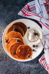 Cottage cheese pancakes with sour cream and berries on a white plate on a blue stone background.