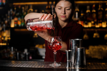 Beautiful female barman pouring sweet red alcoholic drink into a glass