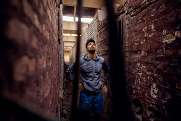 Portrait of focused motivated afro-american young attractive athletic man with earphones standing inside of the abandoned place in the middle of two walls and thinking while looking up.