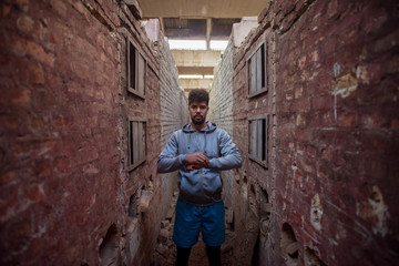 Fototapeta na wymiar Portrait of focused motivated afro-american young handsome sportive man with earphones standing inside of the abandoned place in the middle of two walls and thinking.