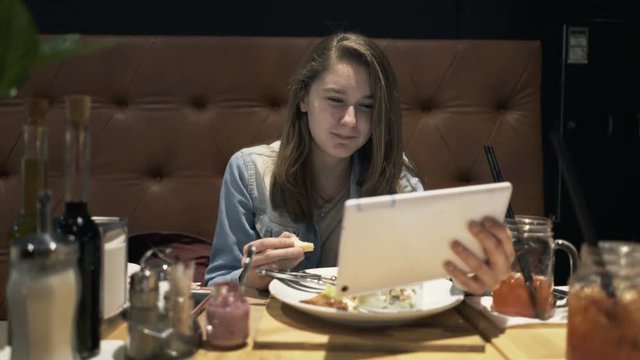 Teenage girl watching movie on tablet during meal sitting by table in cafe
