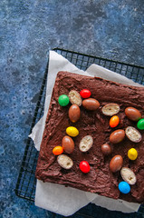 Dark chocolate brownie squares on a wire rack decorated with creamy chocolate eggs. Blue stone...