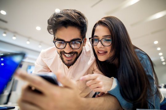 Close up portrait view of adorable happy satisfied hipster young love couple holding and testing new mobile in a tech store.