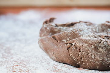 Chocolate dough for cakes on a wooden board, sprinkled with wheat flour