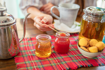 Woman eating homemade strawberry jam. Tea pot, honey, muffins on table