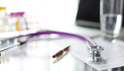 closeup of the desk of a doctors office with a stethoscope in the foreground and a bottle with pills in the background