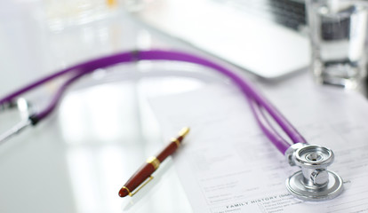 closeup of the desk of a doctors office with a stethoscope in the foreground and a bottle with pills in the background