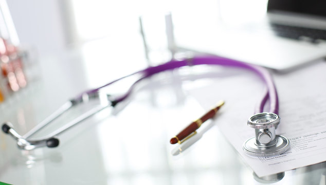 closeup of the desk of a doctors office with a stethoscope in the foreground and a bottle with pills in the background