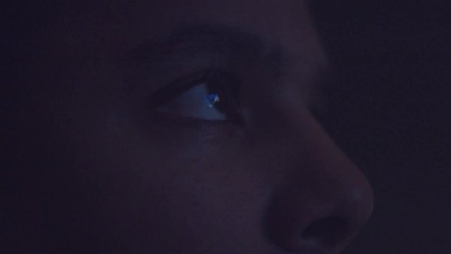upset boring mixed race man watching tv in darkness with different color light from tv on face. Eyes closeup