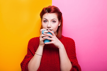 Beautiful girl drinking coffee from a blue mug on two colored background in yellow and pink