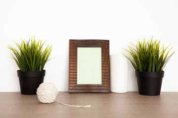 Photo frame next to a candle and two pots with grass over white wall