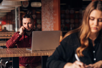 business young girl writing note in notebook in cafe, man with laptop on background