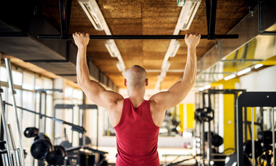 Close up back view of motivated and focused strong muscular active healthy young bald man working pull ups in the modern gym.