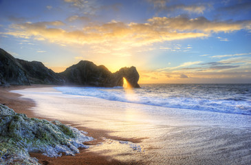 Fototapeta premium Landscape image of sunrise shining through the arch of Durdle Door on the Jurassic Coast