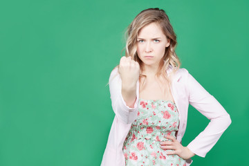 Outraged furious fragile cute woman threatens with fist, has quarrel, screams in terror, shows strength. Irritated annoyed bearded European female being crazy, isolated over green studio wall.