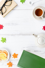 Feminine desk workspace flat lay with diary, eyeglasses, book, tea mug, sweets and felt decor.