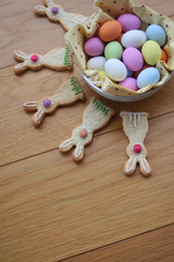 Decorated Easter cookies in shape of bunny with multi colored chocolate eggs on wooden table